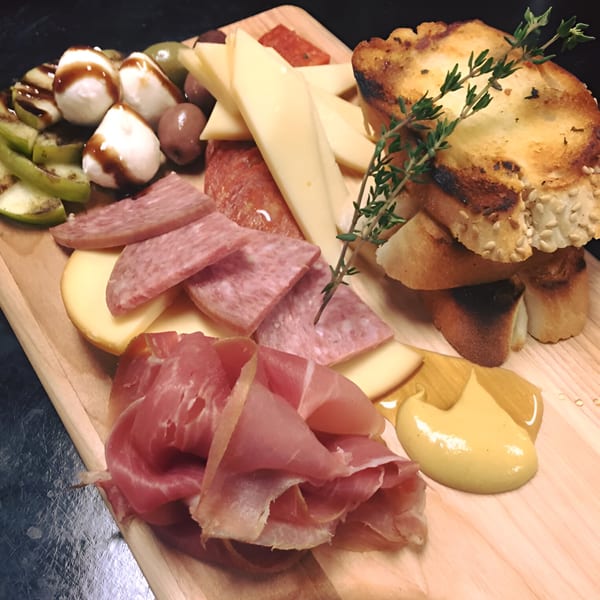 A wooden board with various cheeses, cured meats, olives, mozzarella, and toasted bread.