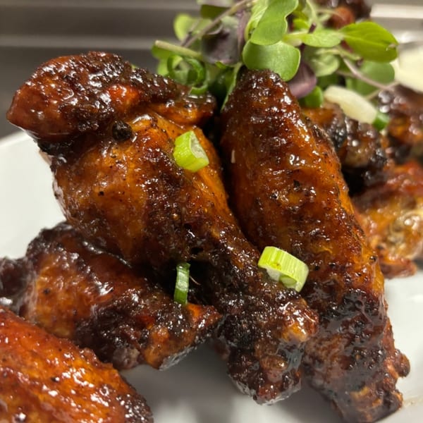 Close-up of glossy, dark brown chicken wings garnished with green onions and microgreens.