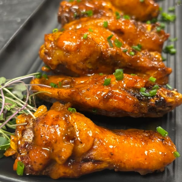 Four glazed chicken wings with chopped chives on a black plate at Casey's Drexel Hill.