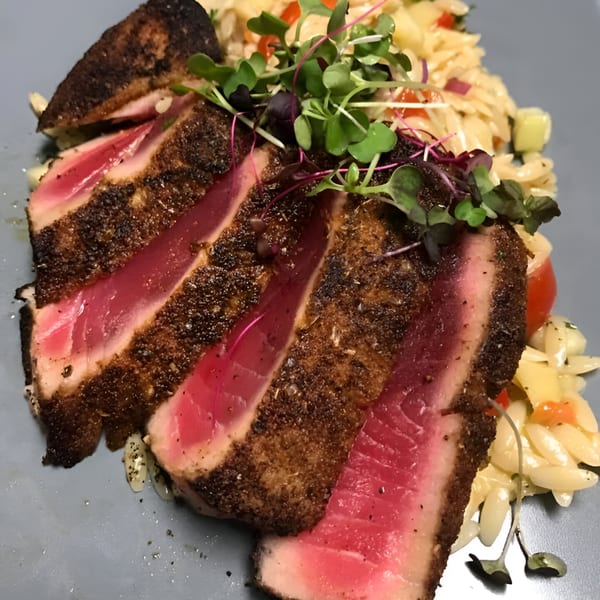 Seared tuna slices with a dark crust, pink center, served with orzo pasta and microgreens.