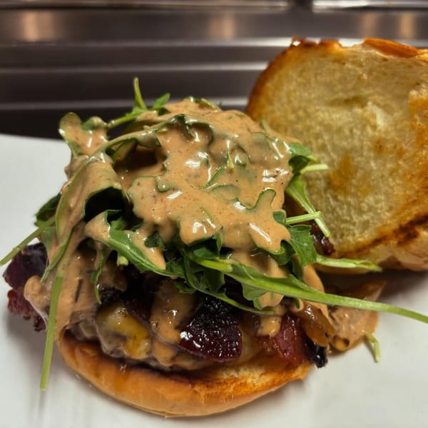 A close-up of a burger with arugula, caramelized onions, and a creamy sauce on a toasted bun.