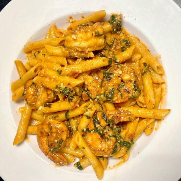 Penne pasta with shrimp, creamy orange sauce, and green herbs in a white bowl.